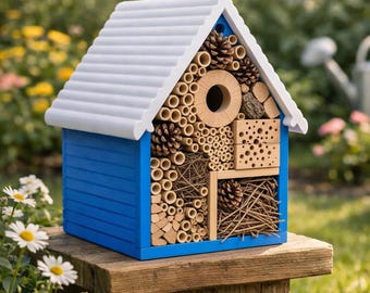 Puede incluir: Una casa de insectos de madera azul y blanca con tejado a dos aguas. La casa está llena de materiales naturales como bambú, piñas y trozos de madera. Está diseñada para proporcionar refugio a los insectos.