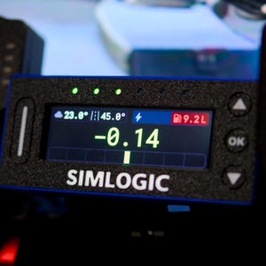 May include: A rectangular black Simlogic digital display unit with a textured finish. The screen shows a central green -0.14 value, a 23.0 degree temperature, 45.0 degree track temperature, and 9.2L fuel level. It features side buttons and arrows.