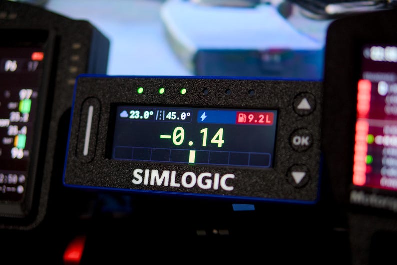 May include: A rectangular black Simlogic digital display unit with a textured finish. The screen shows a central green -0.14 value, a 23.0 degree temperature, 45.0 degree track temperature, and 9.2L fuel level. It features side buttons and arrows.