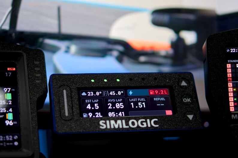 May include: A black Simlogic digital dashboard display unit featuring a rectangular screen with illuminated data metrics including 23.0 degrees, 45.0 degrees, 9.2L fuel, 4.5 est lap, 2.05 avg lap, and 1.51 last fuel, with three green status lights above.
