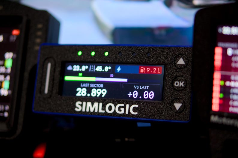 May include: A black rectangular Simlogic digital telemetry display unit with a textured finish. The screen shows data including 23.0 degrees, 45.0 degrees, 9.2L fuel, a last sector time of 28.899, and a vs last value of +0.00 with navigation buttons.