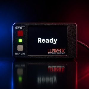 以下が含まれることがあります： 黒い長方形のLumirankドライバー情報ディスプレイ。画面には「Ready」の文字が表示されています。ディスプレイには3つのインジケーターライトがあり、前面には「RCF VIO」と「SFS」の文字があります。ディスプレイは黒いケーブルに接続されています。