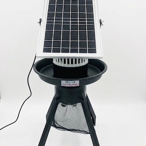 May include: A black solar-powered insect trap with a rectangular solar panel, a white cylindrical component, and a black tray. The trap is supported by a black tripod base and has a mesh net. The text "SAMURAI" is visible.