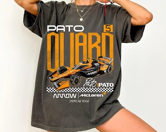 May include: A charcoal gray short-sleeve t-shirt featuring a large graphic of an orange and black IndyCar race car. The design includes the text PATO O'WARD, the number 5, and the Arrow McLaren Indycar Team logo with a checkered flag pattern.