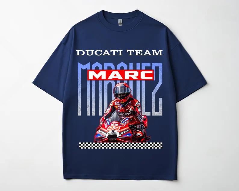 May include: A navy blue short-sleeve t-shirt featuring a graphic print of a motorcycle racer in red gear on a red motorcycle. The text reads DUCATI TEAM, MARC in a red box, and MARQUEZ in large light blue letters, with a black and white checkered border.
