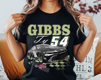 May include: A black short-sleeve t-shirt featuring a graphic of a black race car with the number 54. The text GIBBS, Ty, and 54 are printed in large white and light green lettering above the car, with a checkered pattern design below the vehicle.
