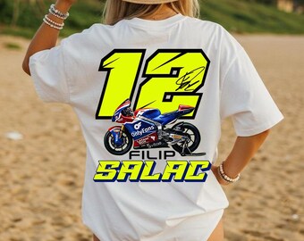May include: A white short-sleeve t-shirt featuring a large neon yellow number 12 on the back, a graphic of a blue and red racing motorcycle, and the text Filip Salac in bold yellow letters with a blue outline, including a signature graphic.