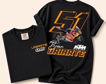 May include: A black t-shirt featuring a small orange and white logo on the front chest that reads URIARTE AJO motorsport. The back displays a large orange number 51, a Red Bull KTM racing motorcycle, the name Brian URIARTE, and KTM RACING text.