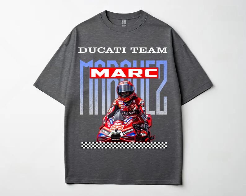 May include: A dark gray short-sleeve t-shirt featuring a graphic print of Marc Marquez on a red Ducati motorcycle. The text DUCATI TEAM appears at the top, with MARC MARQUEZ in large letters behind the rider. A black and white checkered pattern is at the base.