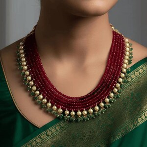 May include: A multi-strand necklace featuring five rows of deep red faceted beads. The necklace is accented with small cream-colored pearls and tiny green beads arranged in a repeating pattern along the lower edge of the strands.