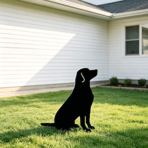 May include: A solid black silhouette of a dog in a sitting position, featuring a distinct outline of a canine head with a pointed ear and a long tail, positioned upright on a flat surface to create a decorative garden or lawn ornament.