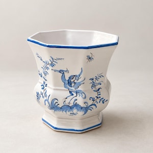 May include: A white ceramic planter with an octagonal shape and a blue rim. The exterior features hand-painted blue illustrations of a crane-like bird, foliage, and a small butterfly. The base is also octagonal, matching the top opening design.
