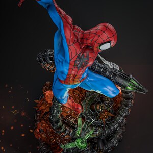 May include: A dynamic statue of Spider-Man in a classic red and blue suit, mid-action. The figure is posed above a detailed, mechanical base with green and black accents, set against a dark background. The statue captures the essence of the superhero.