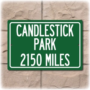 May include: Green metal sign with white text that reads "Candlestick Park 2150 Miles".