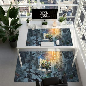 May include: A white desk with a computer, keyboard, mouse, and headphones. A large desk mat and a smaller rug feature a detailed illustration of a rainy street scene with cartoon characters. The text "DESK ORA:" is on the computer screen.