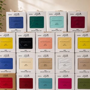 May include: Stacked boxes of organic sheet sets in various colors, including blue, green, yellow, and pink. Each box displays the sheet color and the "TREE organic" logo. The boxes are arranged in a neat display, showcasing the variety of available sets.