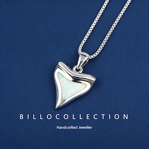 May include: A silver pendant necklace featuring a shark tooth design. The pendant has a white opal centre and hangs from a fine silver chain. The text "BILLOCOLLECTION" and "Handcrafted Jeweller" are at the bottom.