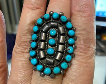 May include: A silver ring with a turquoise stone setting. The ring is oval shaped and has a cluster of turquoise stones in the centre.