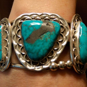 May include: A silver bracelet with three turquoise stones set in intricate silver designs. The stones are a vibrant blue-green color and are surrounded by delicate silver filigree.