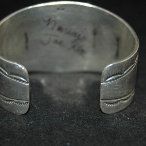 May include: Silver cuff bracelet with a Native American design. The bracelet is stamped with the maker's mark "Navajo Joe K" on the back.