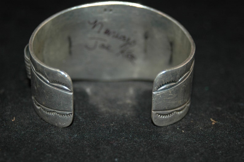 May include: Silver cuff bracelet with a Native American design. The bracelet is stamped with the maker's mark "Navajo Joe K" on the back.