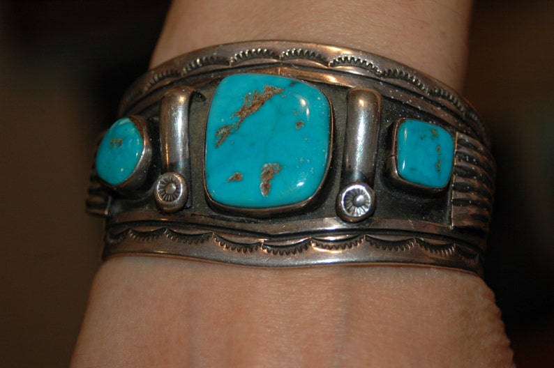 May include: A silver bracelet with turquoise stones. The bracelet features a decorative design and is worn on a person's wrist.