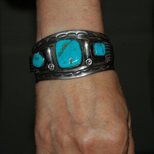 May include: A silver bracelet with turquoise stones set in a silver band. The bracelet is worn on a person's wrist.