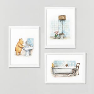 May include: Three framed watercolour prints showing bathroom scenes with cartoon characters. One shows a bear washing its paws, another a pig near a toilet, and the last a bathtub scene with a bear and a child. The prints are in white frames.