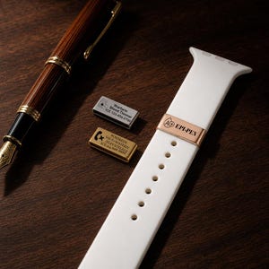 May include: A white silicone watch band featuring a rose gold medical alert charm engraved with "A+ EPI-PEN". Two additional rectangular metal medical alert charms are present, one silver with "Warfarin Blood Thinner" and one gold with "POST&EDS".