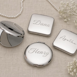 May include: A collection of silver-toned metal compact mirrors in square and round shapes. Two square mirrors are engraved with the names Dana and Agatha, while one round mirror is engraved with the name Henry. One round mirror is shown open.