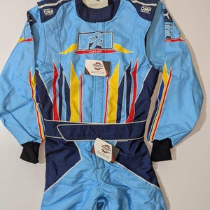 May include: Light blue racing suit with the text "FA RACING KART". The suit has yellow, red, and blue accents, with "OMP" logos on the shoulders. It features a dark blue collar, waist belt, and cuffs.
