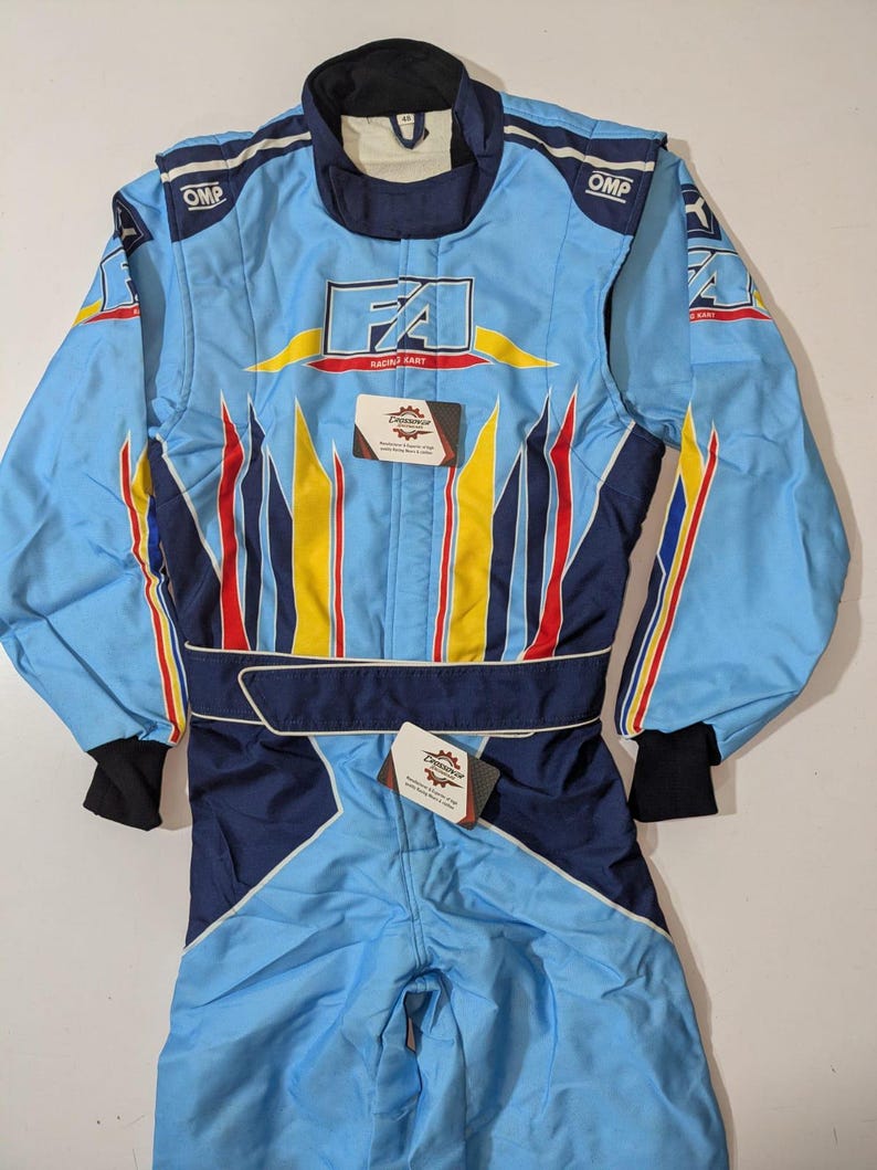May include: Light blue racing suit with the text "FA RACING KART". The suit has yellow, red, and blue accents, with "OMP" logos on the shoulders. It features a dark blue collar, waist belt, and cuffs.