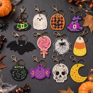 May include: A collection of twelve embroidered Halloween-themed keychains featuring various designs including a witch hat, ghost, jack-o'-lantern, bat, lollipop, spider web, candy corn, cauldron, wrapped candy, skull, and a crescent moon.