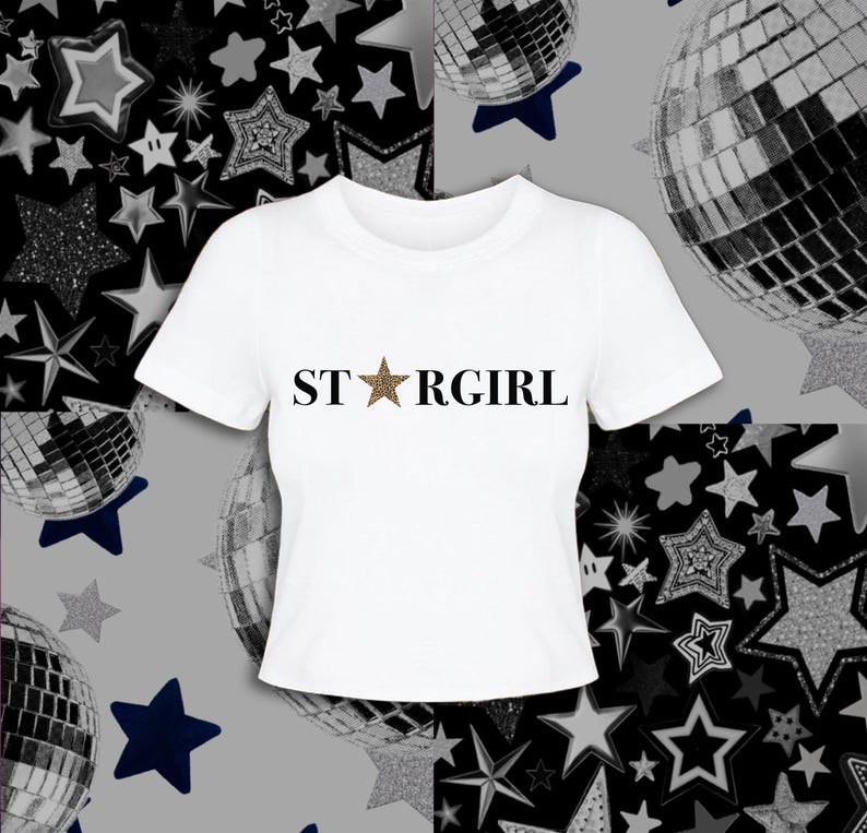 Puede incluir: Una camiseta blanca de manga corta con el texto negro "STARGIRL" impreso en el pecho, donde la letra "A" est&aacute; sustituida por una estrella de cinco puntas con un estampado de leopardo marr&oacute;n y negro en su superficie.