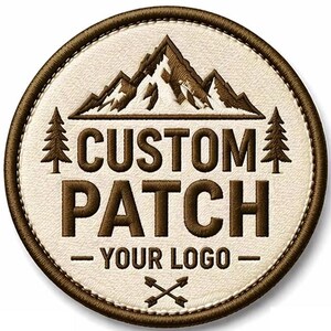 Peut inclure: Écusson rond brodé avec une chaîne de montagnes, deux pins et l'inscription "CUSTOM PATCH - YOUR LOGO -" en marron sur fond crème. Bordure marron cousue et flèches croisées en bas.
