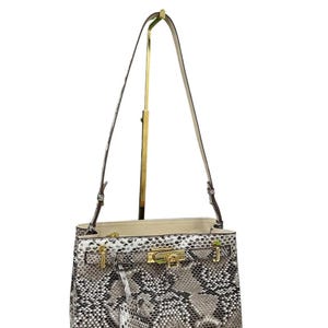 May include: A snakeskin-effect handbag with a gold-tone clasp and fittings. The bag features a top handle and a detachable shoulder strap. The interior is a light beige colour. The bag is displayed on a gold stand.