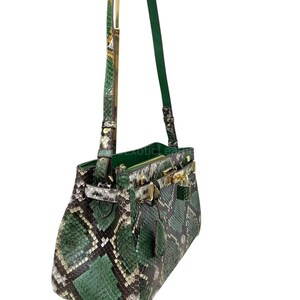 May include: A green and black snakeskin handbag with gold-tone clasps and handle hardware. The bag features a top handle and a long, adjustable shoulder strap. The bag is made of genuine snakeskin and has a structured shape.