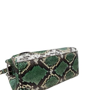 May include: A green and black snakeskin-patterned handbag. The bag features a diamond pattern in shades of green, black, and white. The bag has a rectangular shape with a handle and a clasp.