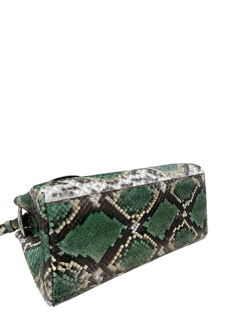 May include: A green and black snakeskin-patterned handbag. The bag features a diamond pattern in shades of green, black, and white. The bag has a rectangular shape with a handle and a clasp.