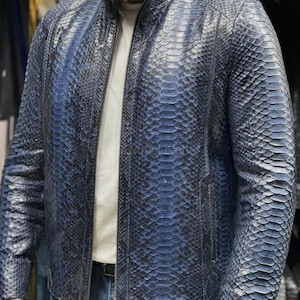 Może przedstawiać: Niebieska skórzana kurtka ze wzorem skóry węża. Kurtka ma zapięcie na zamek błyskawiczny i stójkę. Kurtka jest noszona na białym t-shircie i niebieskich dżinsach.