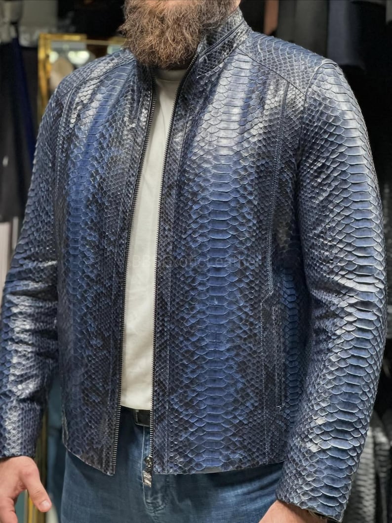 May include: A blue leather jacket with a snakeskin pattern. The jacket has a zipper closure and a stand-up collar. The jacket is worn over a white t-shirt and blue jeans.