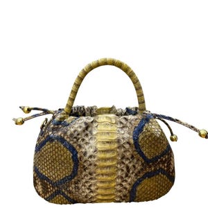 May include: A small, round handbag with a snakeskin pattern in shades of tan, brown, and blue. The bag has a curved handle and drawstring closure with gold-coloured accents. The bag's design features a unique texture and colour palette.