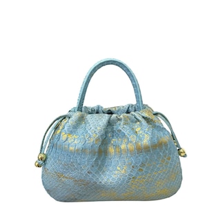 Peut inclure: Un sac à main bleu clair avec un motif peau de serpent et des accents dorés. Le sac a une fermeture à cordon et une poignée supérieure. Le sac mesure environ 25 cm de large et 20 cm de haut.