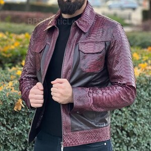 May include: A burgundy leather jacket with a snakeskin pattern. The jacket features a collared neckline, two chest pockets, and a zip closure. The text "BBS Exotic Leather" is visible on the upper left side.