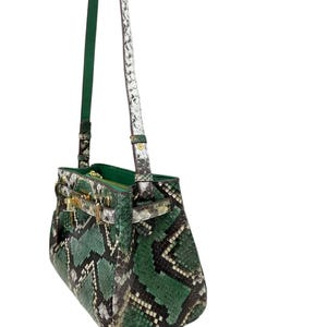 May include: A green and black snakeskin-patterned handbag with gold-coloured clasp and hardware. The bag has a top handle and a long, detachable shoulder strap. The interior is green. The bag is made of a snakeskin material.