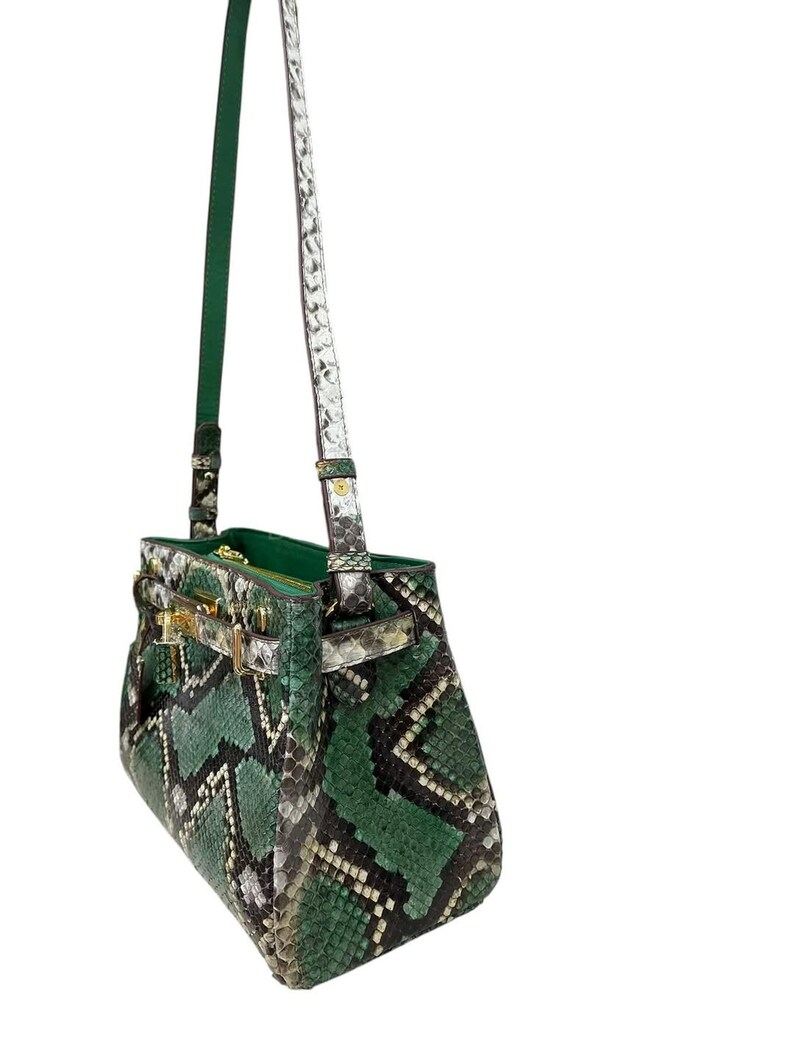 May include: A green and black snakeskin-patterned handbag with gold-coloured clasp and hardware. The bag has a top handle and a long, detachable shoulder strap. The interior is green. The bag is made of a snakeskin material.