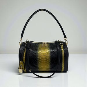 Könnte beinhalten: Schwarz-goldene Handtasche mit Schlangenmuster, mit einem oberen Griff und einem abnehmbaren Schulterriemen. Die Tasche verfügt über einen goldenen Reißverschluss, goldfarbene Hardware und ein kleines Schlossdetail. Die Tasche hat eine zylindrische Form.