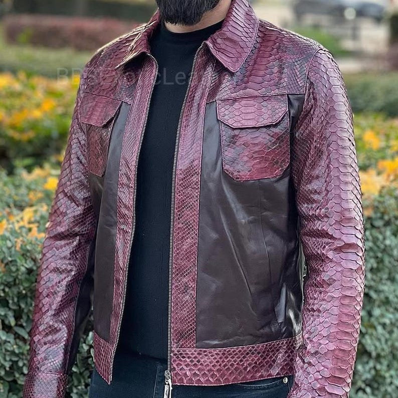 May include: A burgundy and brown leather jacket with a snakeskin pattern. The jacket has two chest pockets, a zip closure, and a collared neckline. The sleeves and shoulders feature the snakeskin pattern, while the body is a solid brown colour.