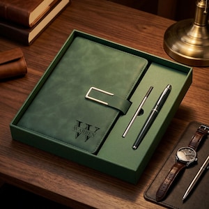 May include: A green leather journal with a silver clasp, a pen, and a pen in a green box. The journal has the name "WARREN" printed on it. A watch with a brown leather strap is also visible.