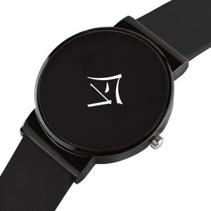 Puede incluir: Reloj de pulsera negro con esfera redonda y correa negra. La esfera del reloj presenta un s&iacute;mbolo blanco. El reloj tiene una corona plateada. El reloj es de dise&ntilde;o minimalista.